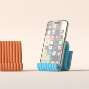 May include: A blue and orange phone stand with a modern design. The blue stand holds a smartphone, displaying app icons on the screen. The orange stand is a similar design, but is not holding a phone. The background is a solid, neutral colour.
