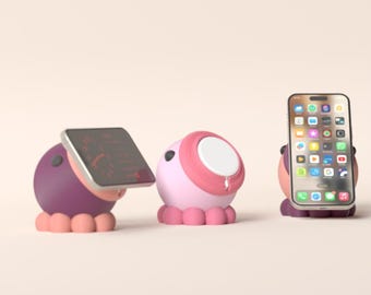 May include: Three octopus-shaped phone stands in purple, pink, and dark purple colors. Each stand features rounded tentacles at the base and a flat surface for mounting a smartphone or small digital device. One stand holds a smartphone vertically.