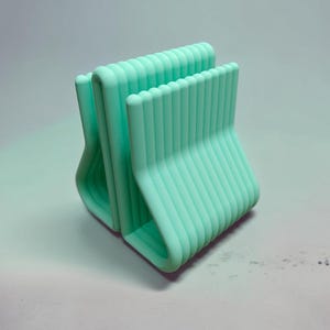 May include: A mint green desk organizer featuring a series of parallel, vertical, rounded bars arranged in a repeating, stepped pattern. The structure is composed of multiple connected U-shaped segments that create a ribbed, textured appearance.
