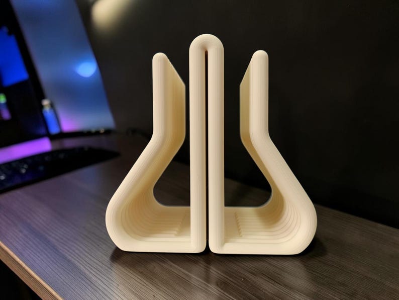 May include: A cream-colored, U-shaped desk organizer featuring a central vertical divider and two symmetrical side compartments with curved, rounded edges. The object has a smooth, matte finish and a structured, open-frame design.