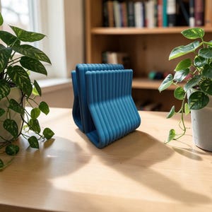May include: A blue desk organizer featuring a series of parallel, rounded vertical ribs connected at the base. The object has a U-shaped profile with a matte finish and is positioned upright, displaying a uniform, ridged texture across its surface.