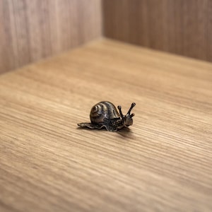 Puede incluir: Una peque&ntilde;a figurita de caracol negra y plateada sobre una superficie de madera.