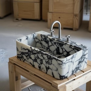 a black and white marble sink with a silver faucet, placed on a wooden stand.