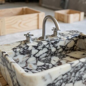 a marble sink with a silver faucet, placed on a wooden stand.