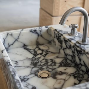 a marble sink with a silver faucet, set against a wooden background.