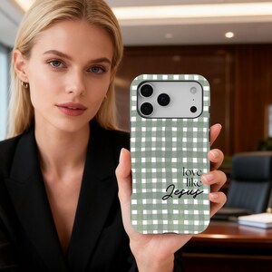 May include: A phone case featuring a green and white gingham design. The case displays the words "love like Jesus" in a handwritten style. The phone case is held by a person.
