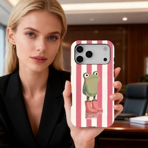 Könnte beinhalten: Smartphone-Hülle mit einem Cartoon-Frosch, der rosa Stiefel trägt, vor einem Hintergrund aus roten und weißen vertikalen Streifen. Die Hülle hat einen Kameraausschnitt und eine glatte, glänzende Oberfläche.