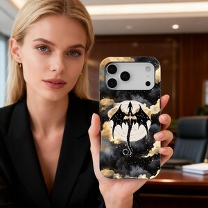 Puede incluir: Funda de teléfono negra y dorada con una silueta de dragón sobre una luna llena y nubes. La funda tiene un acabado brillante y un recorte para la cámara.