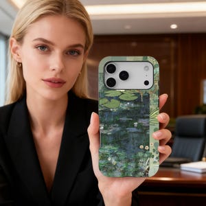 May include: A smartphone case with a painting of water lilies in a pond, in green and blue tones. The case has a protective design and a camera cutout. The case is held by a person.