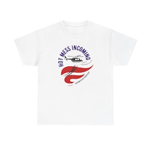 May include: White t-shirt featuring a graphic design with a helicopter and the text "HOT MESS INCOMING". The design includes red, white, and blue elements, with the hashtag #AIRMEDICALTRANSPORT.