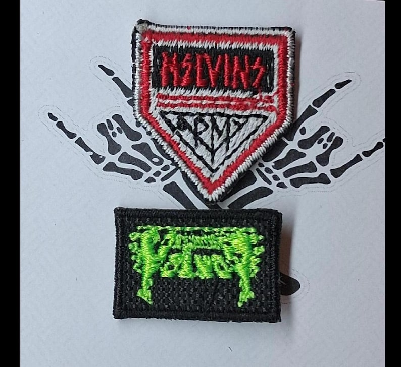 Może przedstawiać: Dwie haftowane naszywki. G&oacute;rna naszywka ma kształt czerwonej, białej i czarnej tarczy z napisami "MELVINS" i "ARMY". Dolna naszywka to czarny prostokąt z zielonym tekstem. Tło przedstawia gest szkieletowej dłoni.