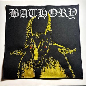 Könnte beinhalten: Schwarzer quadratischer Aufnäher mit dem Wort "BATHORY" in weißen gotischen Buchstaben. Darunter eine gelbe Illustration einer gehörnten Ziege mit roten Augen. Die Ziege blickt nach vorne, ihre Hörner zeigen nach oben.