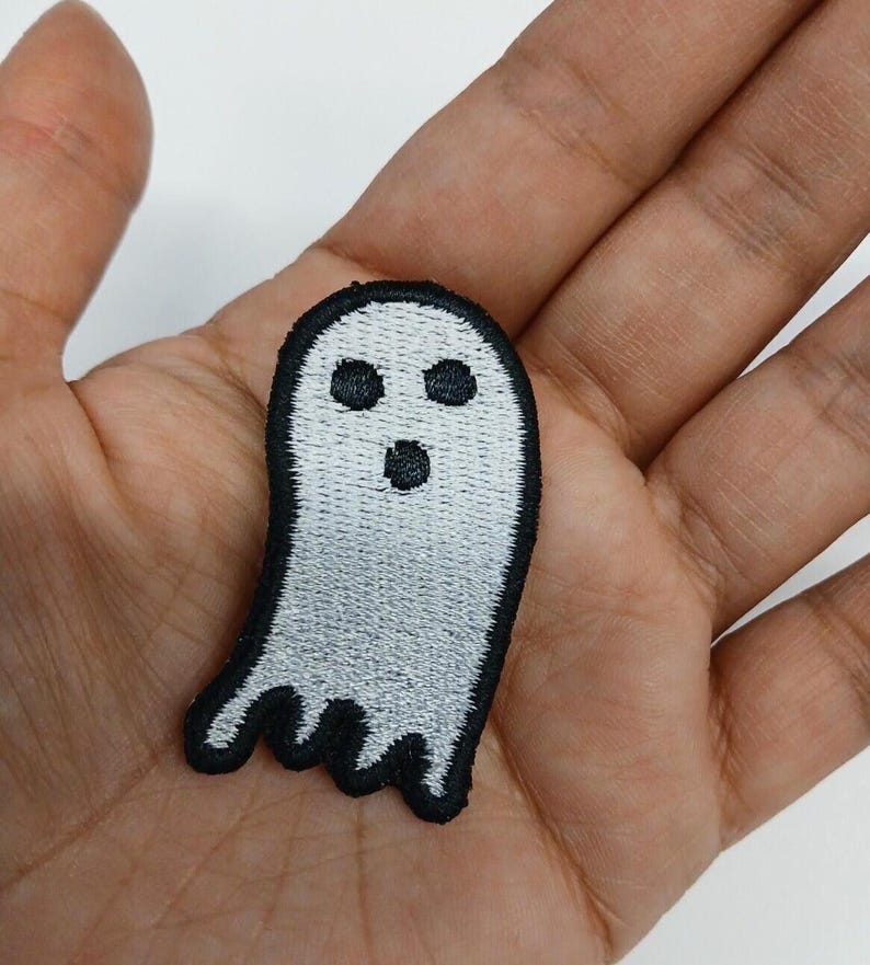 May include: Embroidered ghost patch in white with a black outline. The ghost has three black eyes and a small open mouth. The patch is held in a hand.
