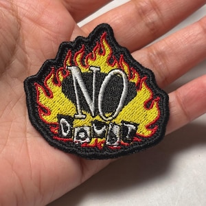 May include: An embroidered patch featuring a yellow and red flame design surrounding the text NO DOUBT in white lettering. The patch has a black border and black background elements, with the word NO in large letters above the word DOUBT.