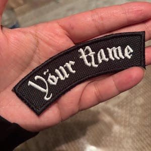Puede incluir: Parche de tela negro con texto bordado en blanco que dice "Your Name".