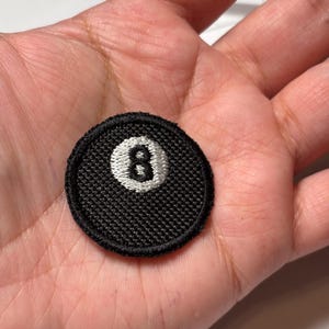 May include: Black and white embroidered patch of a billiard ball with the number 8 on it.