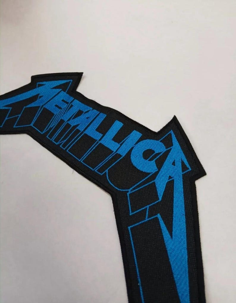 May include: Black and blue embroidered patch with the word "Metallica" in a stylized font.