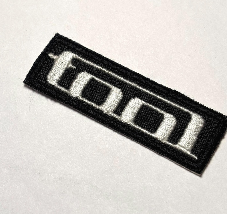 May include: Black fabric patch with white embroidered letters spelling "TOOL" in a stylized font.