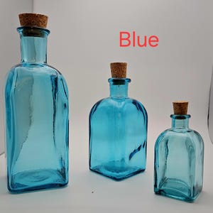 May include: Three blue glass bottles with cork stoppers, in different sizes. The bottles have square or rectangular shapes. The word "Blue" is written in red in the background.