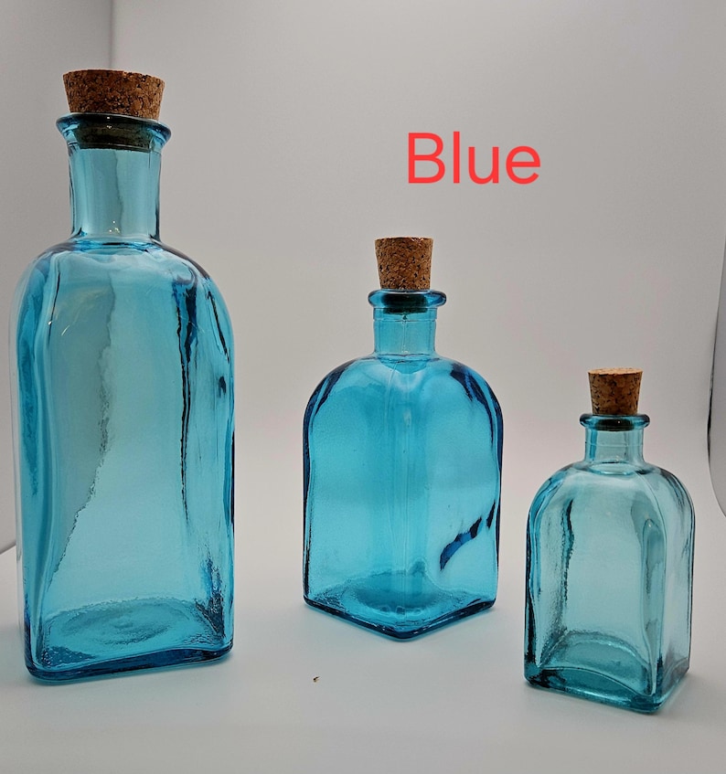 May include: Three blue glass bottles with cork stoppers, in different sizes. The bottles have square or rectangular shapes. The word "Blue" is written in red in the background.