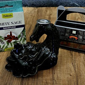 May include: A black incense burner in the shape of a horse, with a box of white sage incense cones and a box of Super Hit incense. The white sage box has the text "White Sage Backflow Incense Cones".