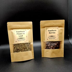 Może przedstawiać: Dwie brązowe torebki typu doypack z papieru kraft z przezroczystymi okienkami. Lewa torebka ma etykietę Hawthorn Flower & Leaf, a prawa Hawthorn Berries. Obie etykiety zawierają grafikę faz księżyca oraz napis Moon Phase Naturals.