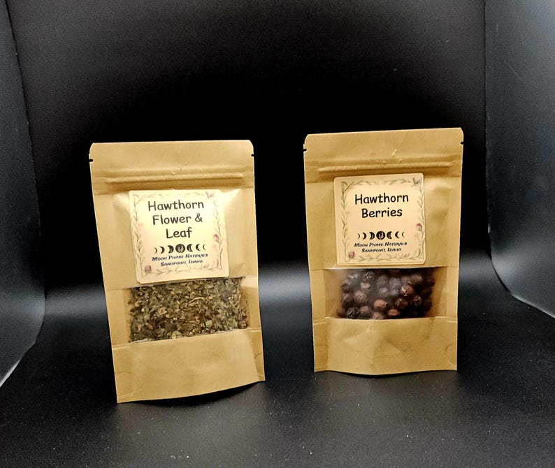 Może przedstawiać: Dwie brązowe torebki typu doypack z papieru kraft z przezroczystymi okienkami. Lewa torebka ma etykietę Hawthorn Flower & Leaf, a prawa Hawthorn Berries. Obie etykiety zawierają grafikę faz księżyca oraz napis Moon Phase Naturals.