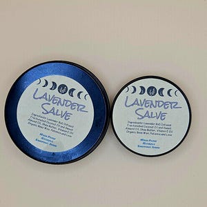 May include: Two round, blue-rimmed tins of Lavender Salve. The labels feature the text "Lavender Salve" in a stylized font, along with ingredient information and a crescent moon design. The tins are of different sizes.