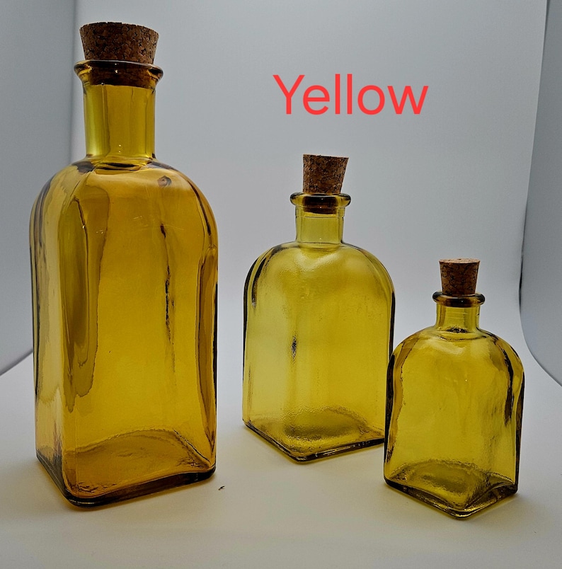 May include: Three yellow glass bottles with cork stoppers. The bottles vary in size, with a rectangular bottle on the left and two rounded square bottles to the right. The word "Yellow" is written in red above the bottles.