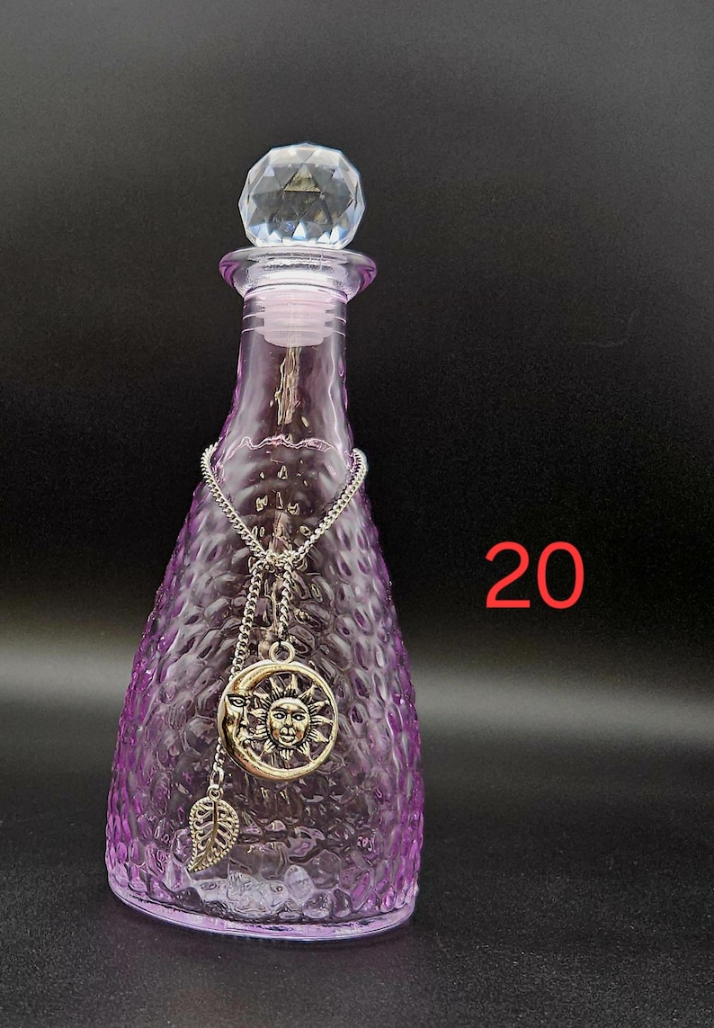 May include: A purple glass bottle with a textured surface and a clear faceted crystal stopper. A silver-toned chain hangs around the neck, featuring a circular sun and moon pendant and a small leaf charm. The number 20 is printed in red on the right.