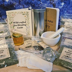May include: A tea blending kit with a guide, honey, and various herbs in clear bags. Includes a mortar and pestle, a metal container, and a tea strainer. The guide is titled "Wild-crafted Tea Blending Guide".