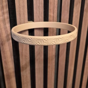 Könnte beinhalten: Ein cremefarbener, kreisförmiger Dekorationsring mit einem sich wiederholenden geometrischen Sternmuster, das um den äußeren Rand geschnitzt ist. Der Ring ist auf einem hölzernen Lattenhintergrund montiert.