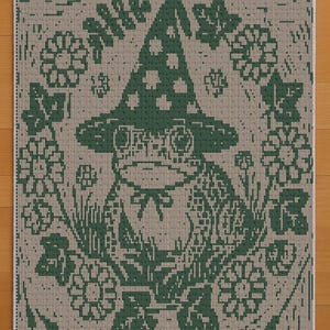 Könnte beinhalten: Ein quadratischer, beige-grüner Teppich mit einem Muster, das einen skurrilen Frosch mit einem Pilzhut zeigt. Der Frosch ist von Blumen und Blättern umgeben. Der Teppich hat ein detailliertes, pixeliges Design.
