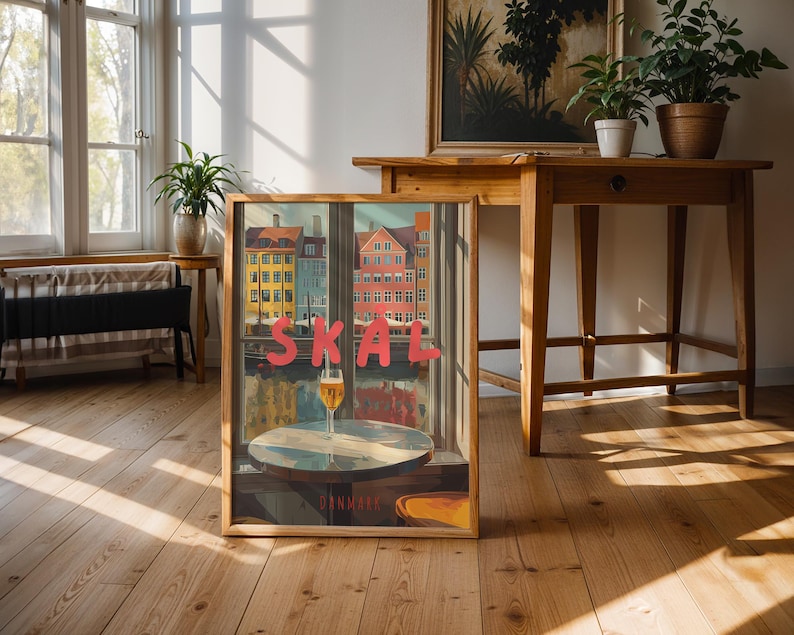 May include: A framed art print featuring a colorful cityscape with the word "SKAL" in red letters. A glass of beer sits on a small table in front of the city view. The word "DANMARK" is at the bottom.