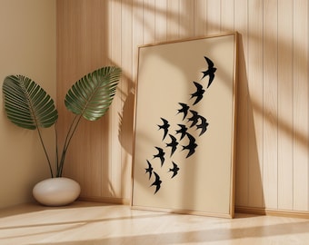 May include: A framed art print featuring a flock of black birds in flight against a beige background. The artwork is displayed in a light brown wooden frame. A potted plant with large green leaves sits nearby, adding a touch of nature to the scene.