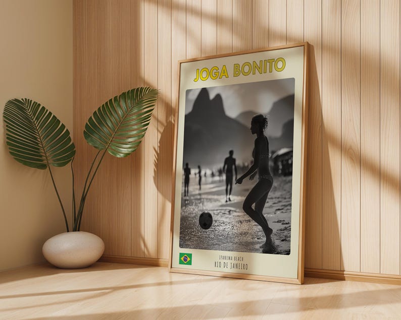 Może przedstawiać: Oprawiony plakat z czarno-białym zdjęciem osoby grającej w piłkę nożną na plaży. Plakat ma u g&oacute;ry ż&oacute;łty napis "JOGA BONITO". Na dole plakatu znajduje się napis "IPANEMA BEACH, RIO DE JANEIRO" oraz brazylijska flaga.