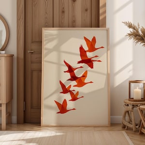 May include: A framed art print featuring a flock of orange geese in flight against a cream background. The artwork is displayed in a light wood frame, adding a touch of warmth to the room's decor. The print is a modern, minimalist design.