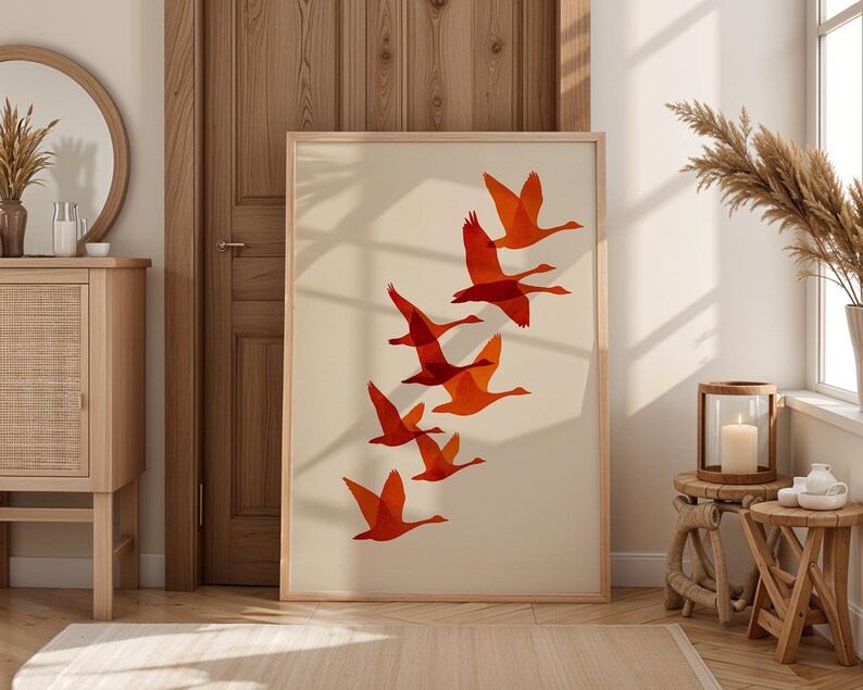 May include: A framed art print featuring a flock of orange geese in flight against a cream background. The artwork is displayed in a light wood frame, adding a touch of warmth to the room's decor. The print is a modern, minimalist design.