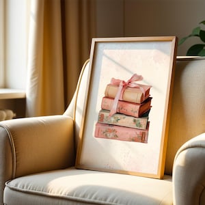 May include: A framed print showing a stack of vintage books in pink and peach hues, adorned with a pink ribbon. The books display floral and textured patterns. The artwork is displayed on a beige armchair near a window.