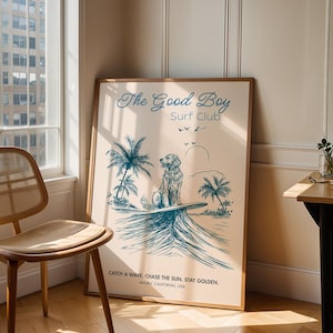 May include: A framed poster with a light beige background features a blue illustration of a dog on a surfboard, palm trees, and the text "The Good Boy Surf Club." The poster includes the text "Catch a wave, chase the sun. Stay golden."