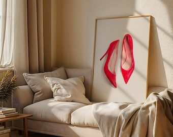 May include: A framed print featuring two bright red high-heeled shoes. The shoes are displayed against a cream-colored background, with a gold frame. The artwork is set in a neutral-toned living room with a sofa and pillows.