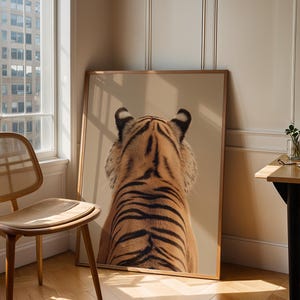 Pode incluir: Uma grande impressão de arte de parede emoldurada de formato retangular apresentando uma ilustração detalhada de um tigre visto por trás. O tigre tem pelo laranja com listras pretas distintas, marcas brancas nas orelhas e pelo branco nas laterais do rosto, sobre um fundo bege sólido.