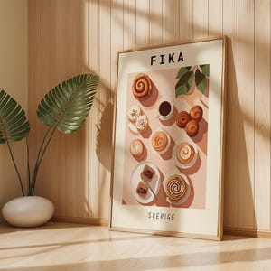 May include: A framed print featuring a still life of pastries and coffee, with the word "FIKA" at the top and "SVERIGE" at the bottom. The image includes cinnamon rolls, cookies, and a cup of coffee on a pink background.