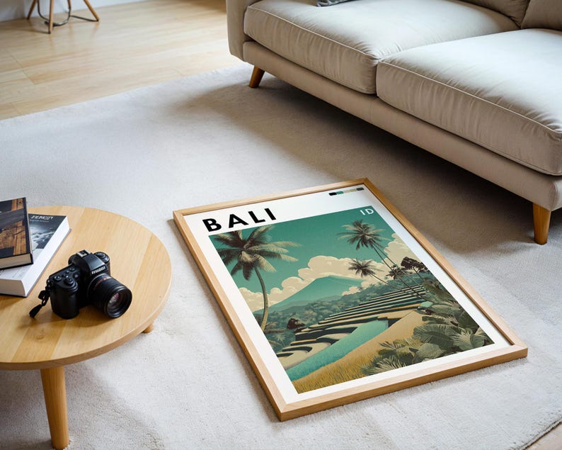 May include: A framed art print featuring a scenic landscape of Bali, Indonesia, with palm trees, terraced rice fields, and a mountain in the background. The word "BALI" is printed at the top. The frame is made of light-colored wood.
