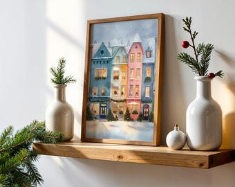 May include: A framed watercolor print of colorful townhouses in a winter scene. The artwork features buildings in shades of blue, yellow, and pink, with snow-covered roofs and festive decorations. The print is displayed on a wooden shelf with decorative vases and greenery.