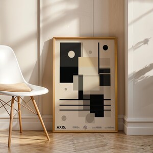 Peut inclure: Une affiche encadrée d'art abstrait avec un cadre doré, présentant des formes géométriques en noir, blanc et beige. Une chaise blanche avec des pieds en bois et un coussin beige est à gauche. L'affiche est appuyée contre un mur.