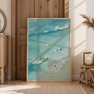 May include: A framed abstract painting of a beach scene with surfers. The artwork features a turquoise ocean with white waves and several surfers riding the waves. The painting is in a light wooden frame.