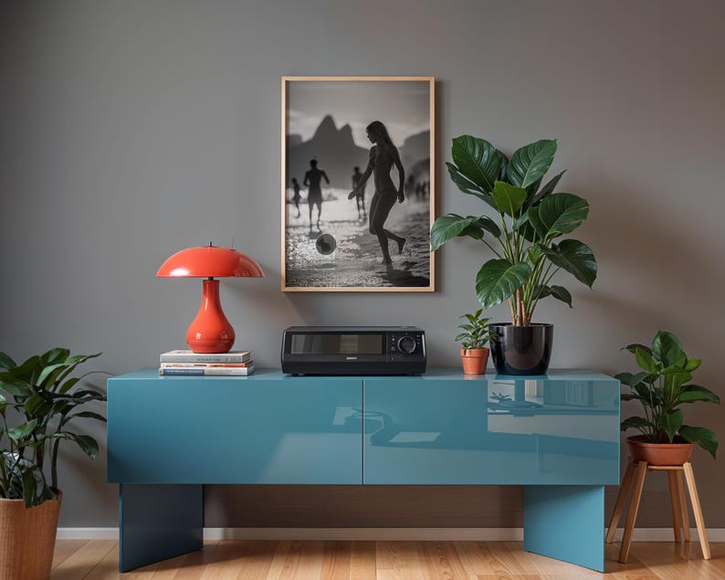 May include: A modern living room scene featuring a teal blue cabinet, a red mushroom-shaped lamp, and a black and white framed photograph. Potted plants and a small stereo system add to the decor.
