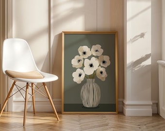 May include: A framed art print featuring a bouquet of white flowers with black centers in a striped vase. The artwork has a gold frame and is set against a muted green background. The print is displayed near a white chair with wooden legs.