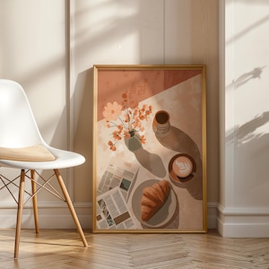 May include: A framed art print depicts a still life with a coffee cup, croissant, vase of flowers, and newspaper. The color palette includes shades of brown, peach, and white. A white chair with a wooden base is in the foreground.